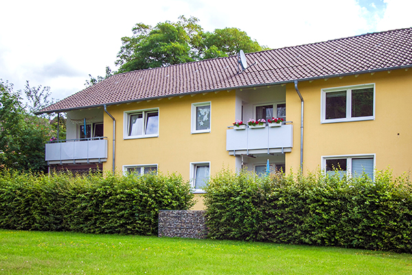Grünanlage mit Hecke vor einem gelben Reihenhaus mit Balkonen