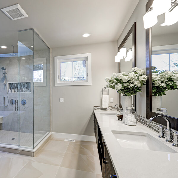 Ein Blick in ein Duschbad mit hellen Fliesen und 2 Spiegeln über 2 Waschbecken