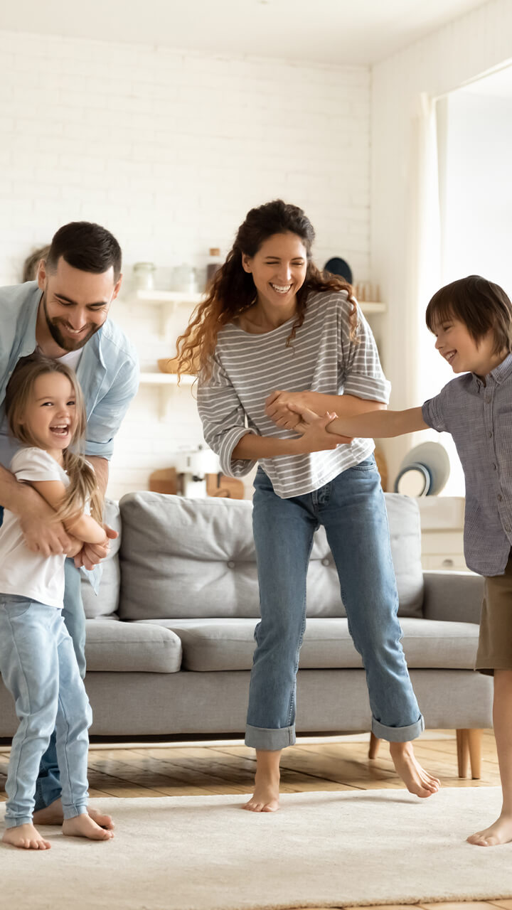Lachende Familie spielt gemeinsam Fangen im Wohnzimmer.