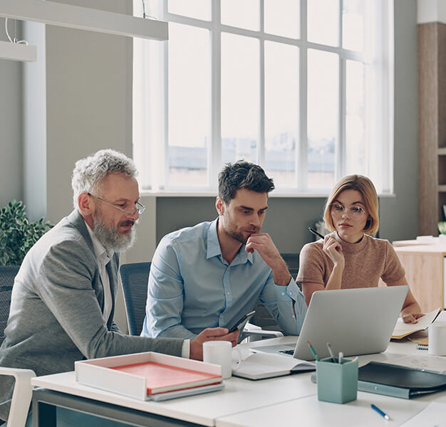 3 Personen sitzen vor einem Laptop und wirken nachdenklich