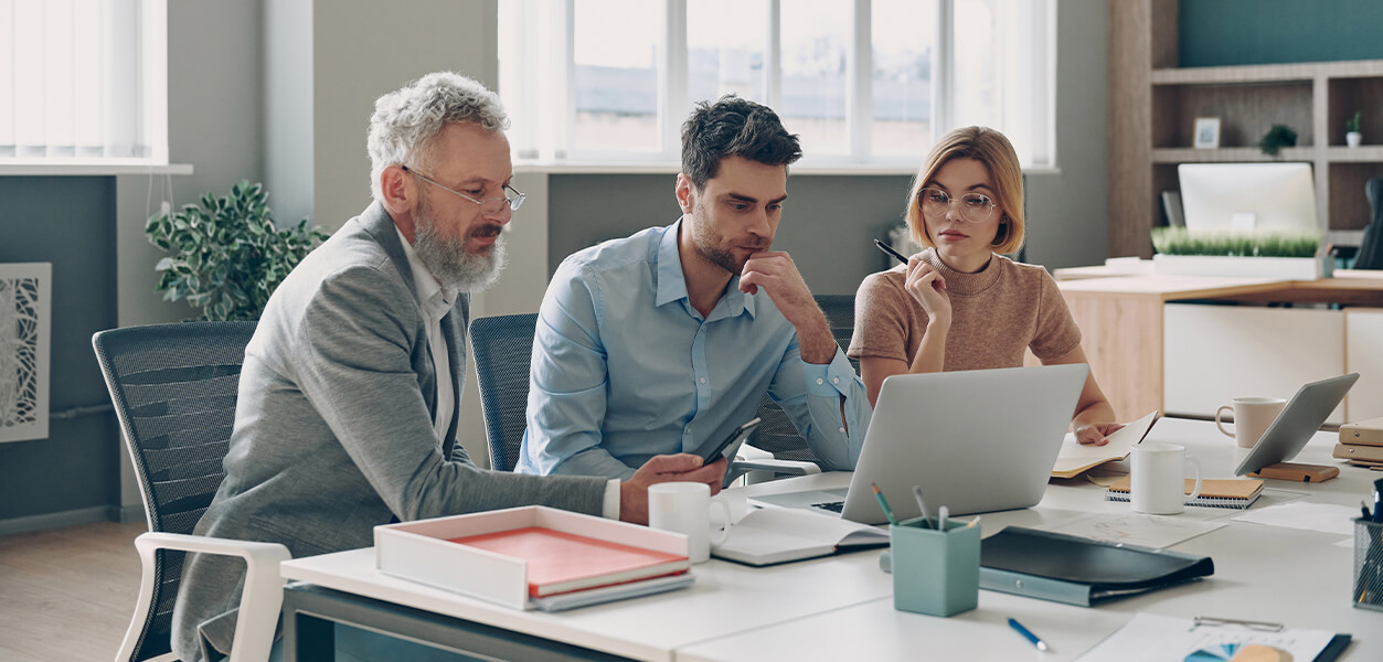 3 Personen sitzen vor einem Laptop und wirken nachdenklich
