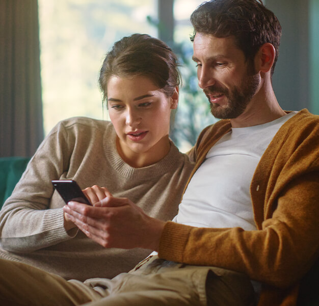 2 Personen sitzen nebeneinander und schauen auf ein Handy